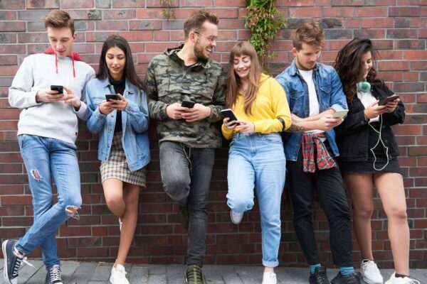Gruppe mit Personen der Generation Z lehnen mit Smartphone in der Hand an einer Wand.