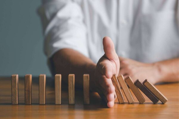 Eine Hand stoppt fallende Dominosteine um einen Konflikt zu symbolisieren.