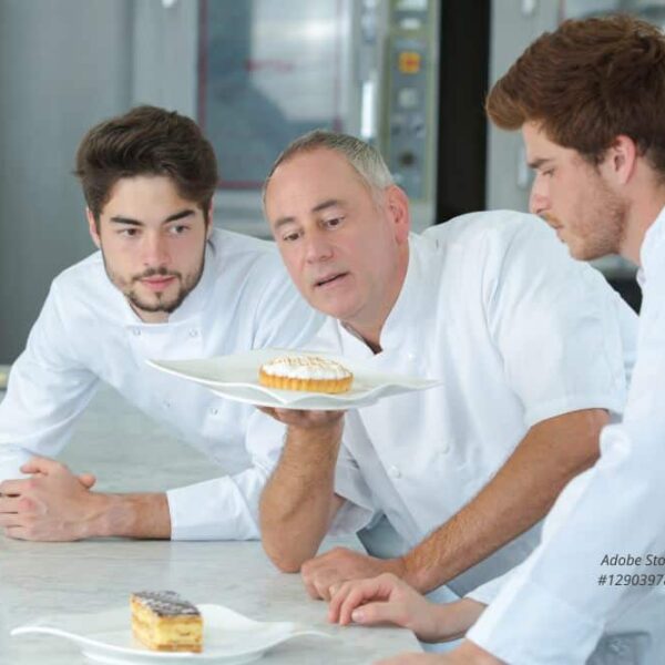 Abbildung: Zwei Auszubildende mit Ihrem Ausbilder betrachten ein Törtchen in der Bäckerei.