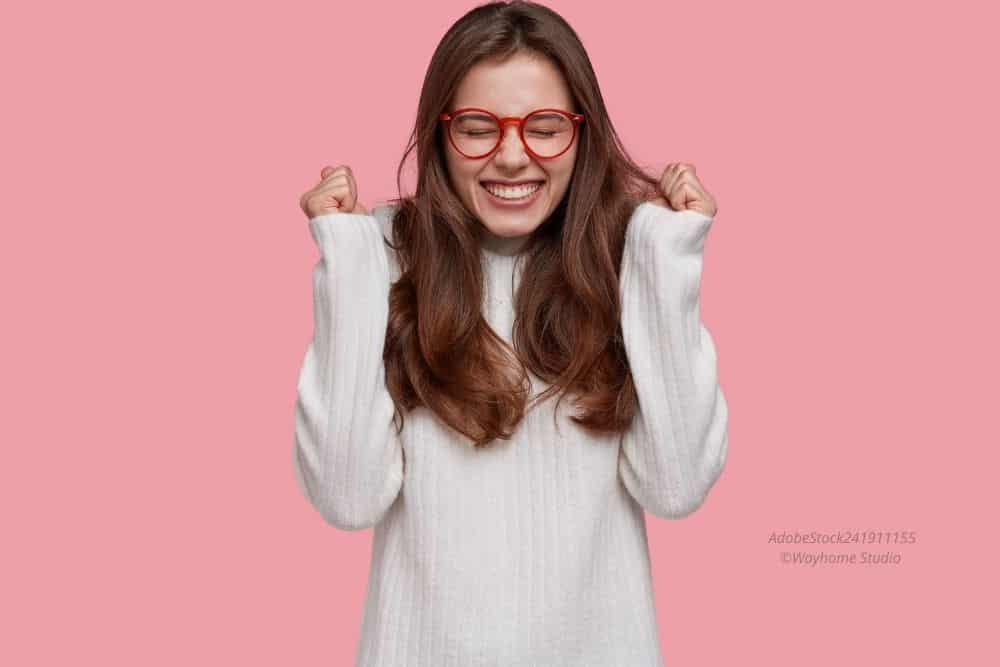 Abbildung: Frau mit Brille und langen Haaren freut sich. Hintergrund pink.